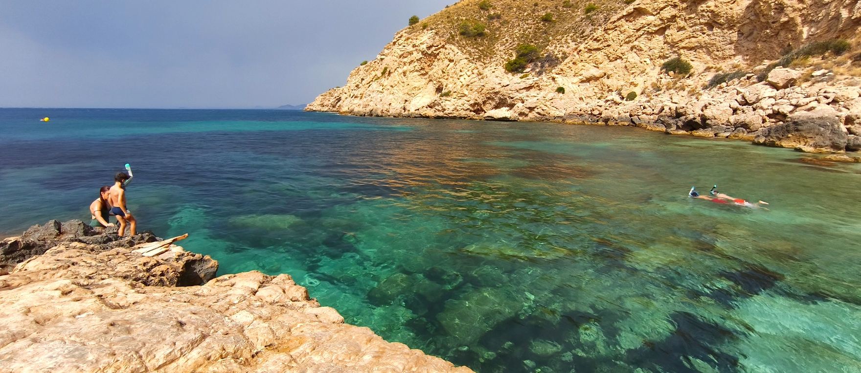 Cala de aguas turquesa en la Costa Blanca con gente haciendo snorkel