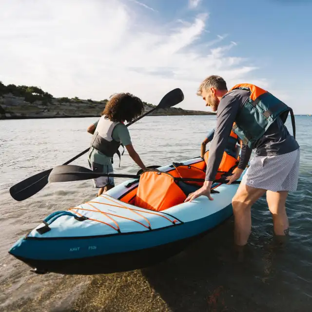 Dos personas botando un kayak hinchable Tribord 100 Essential en la orilla